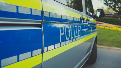 Das Bild zeigt rechte Hälfte eines Polizeiwagens. Silbernes großes Auto mit einem blauen Streifen zwischen zwei neongelben Streifen. In der Mitte steht Polizei.   